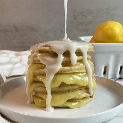 A stack of lemon pancakes, with lemon curd in between each pancake, and lemon glaze being poured on top