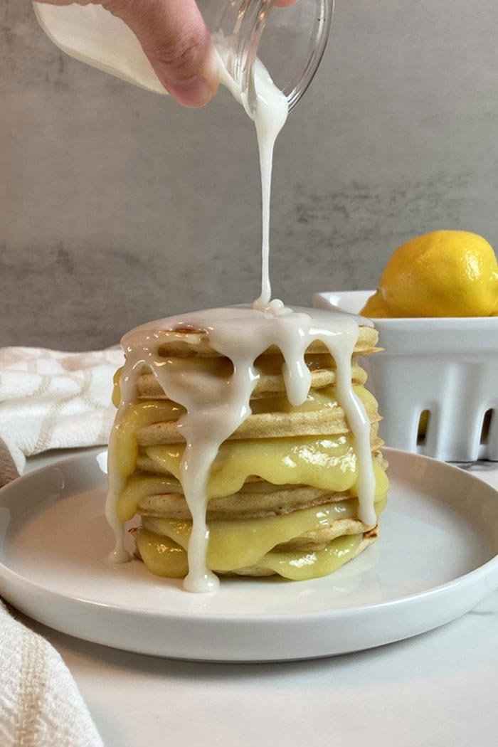 A stack of lemon pancakes, with lemon curd in between each pancake, and lemon glaze being poured on top