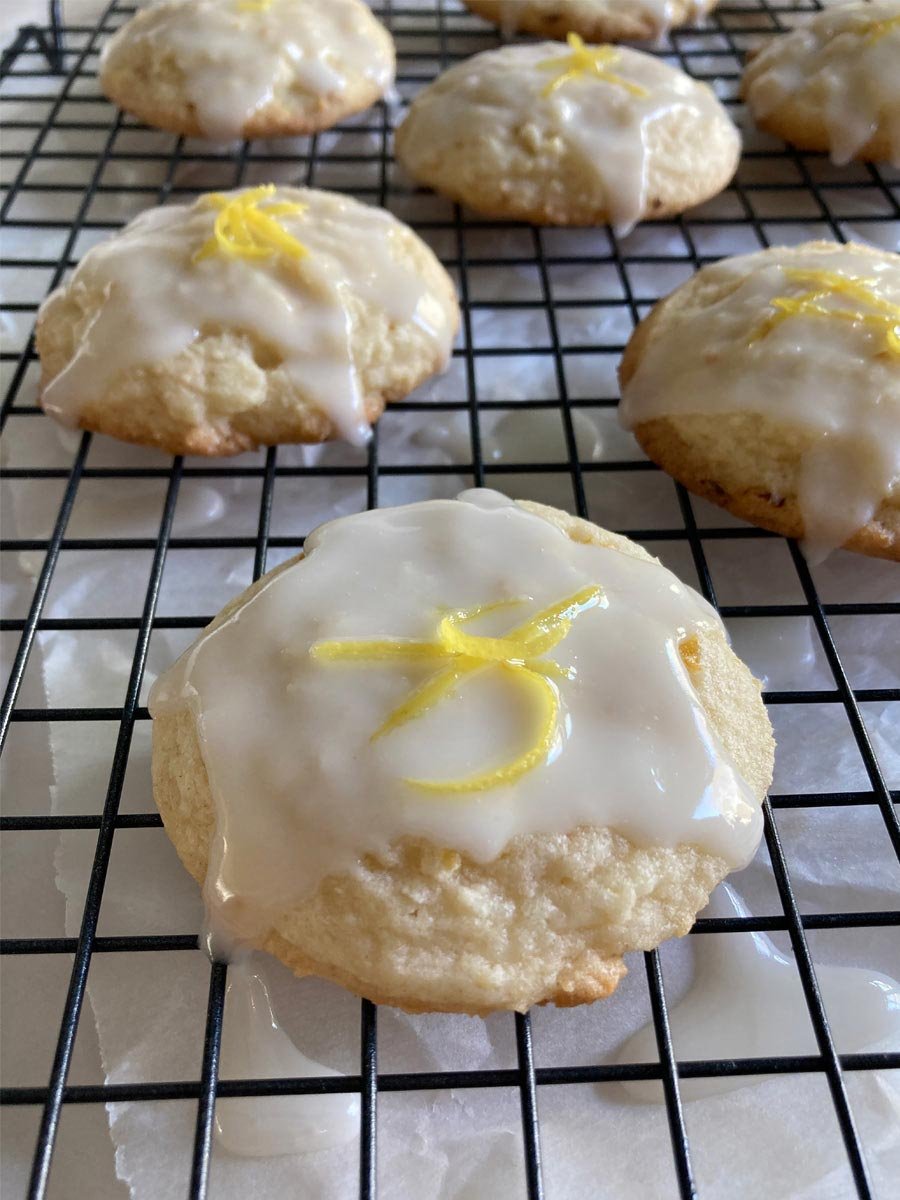 homemade lemon cookies topped with shiny lemon glaze and lemon zest on a cooling rack