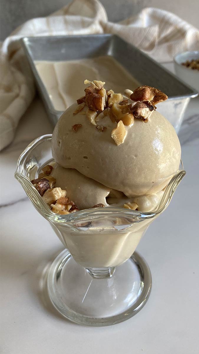 a smooth and creamy scoop of homemade brown sugar walnut ice cream topped with roasted walnut pieces on a marble countertop