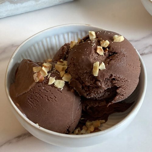 a bowl of homemade chocolate hazelnut ice cream topped with chopped roasted hazelnuts sitting on a marble countertop