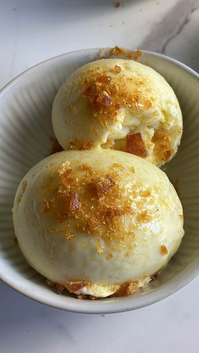 scoop of rich & creamy crème brûlée ice cream with burnt sugar bits sitting in a bowl