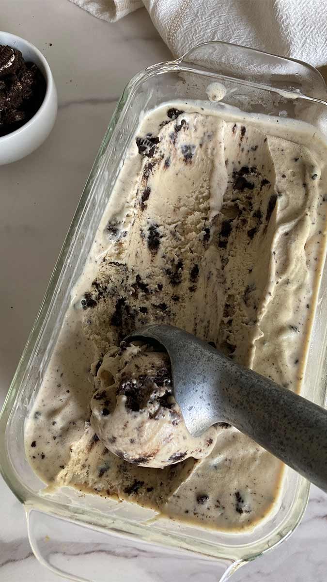 a container of creamy peanut butter cookies and cream ice cream being scooped next to a bowl of Oreo cookie pieces