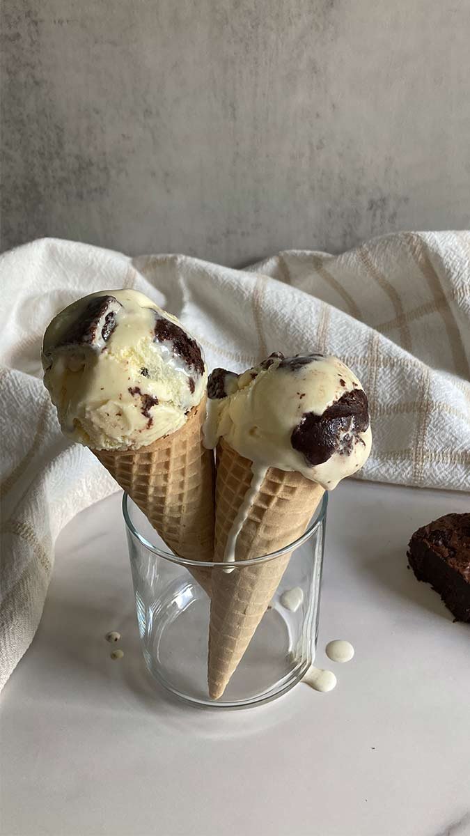 two waffle cones filled with scoops of creamy homemade salted French vanilla brownie ice cream on a marble counter