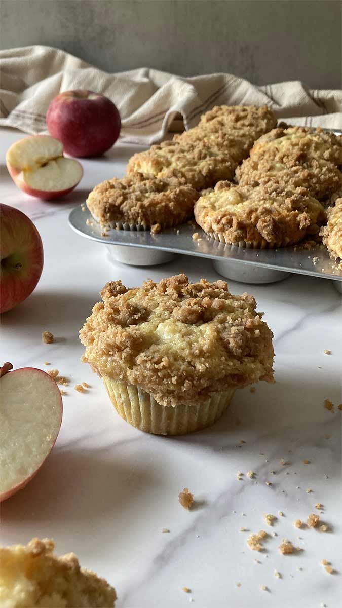 apple muffins with a buttery cinnamon streusel crumble topping on a counter surrounded by apples