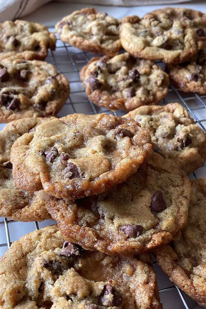 lots of brown butter toffee chocolate chip cookies stacked on a cooling rack