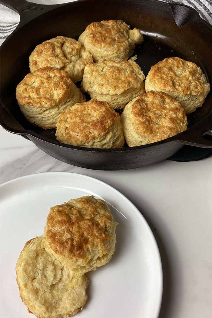 buttermilk biscuits made from scratch in a cast iron skillet with one broken open on a plate to show the tender inside