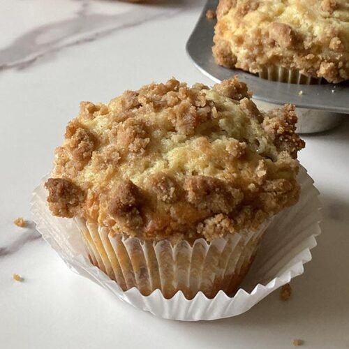 tender pear streusel muffin in a cupcake wrapper sitting on a marble counter