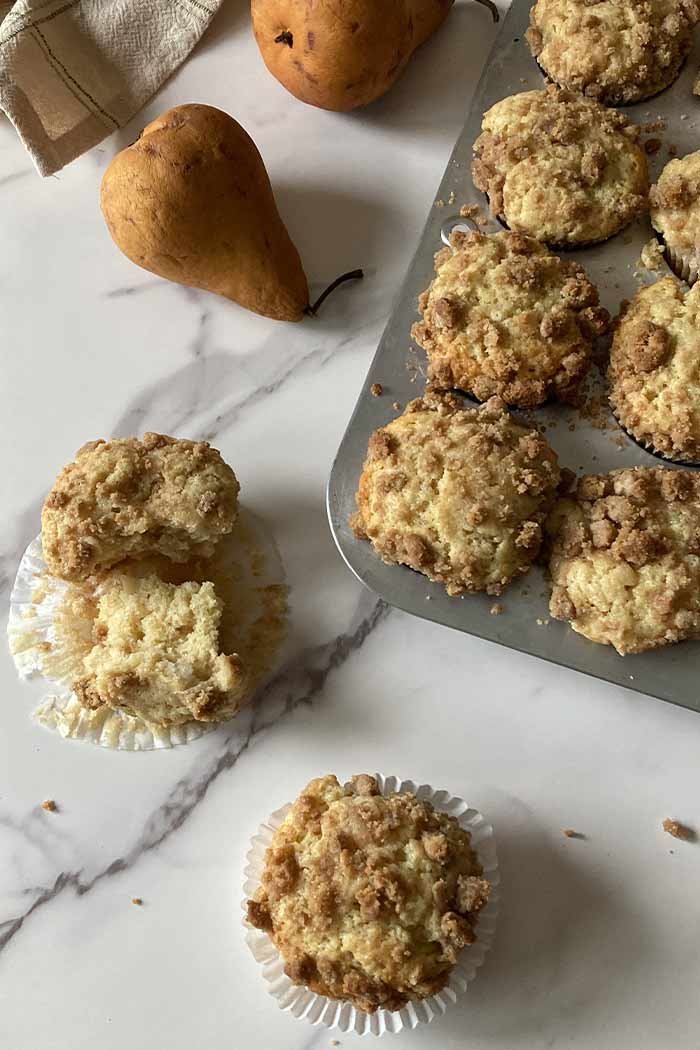 pear streusel muffins in a muffin pan and scattered on a counter surrounded by pears and crumbs
