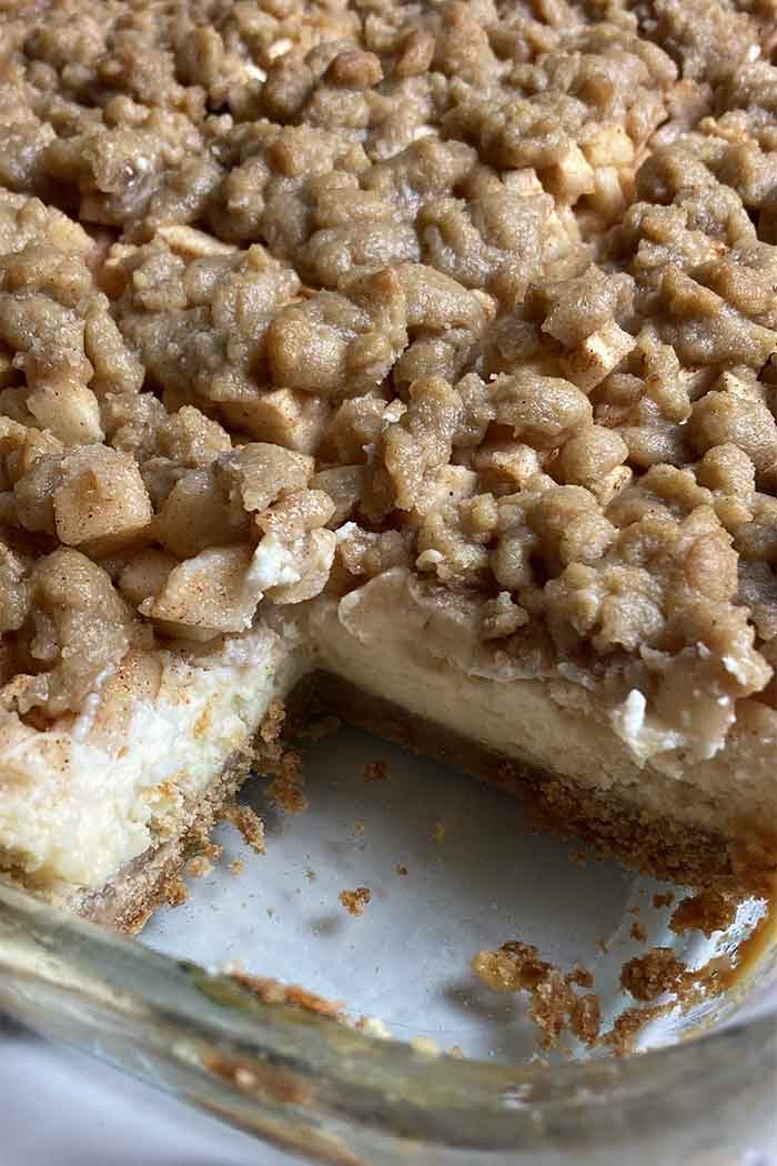 pan of apple crumble cheesecake bars with slice missing showing the crust, cheesecake, apple, and crumble layers
