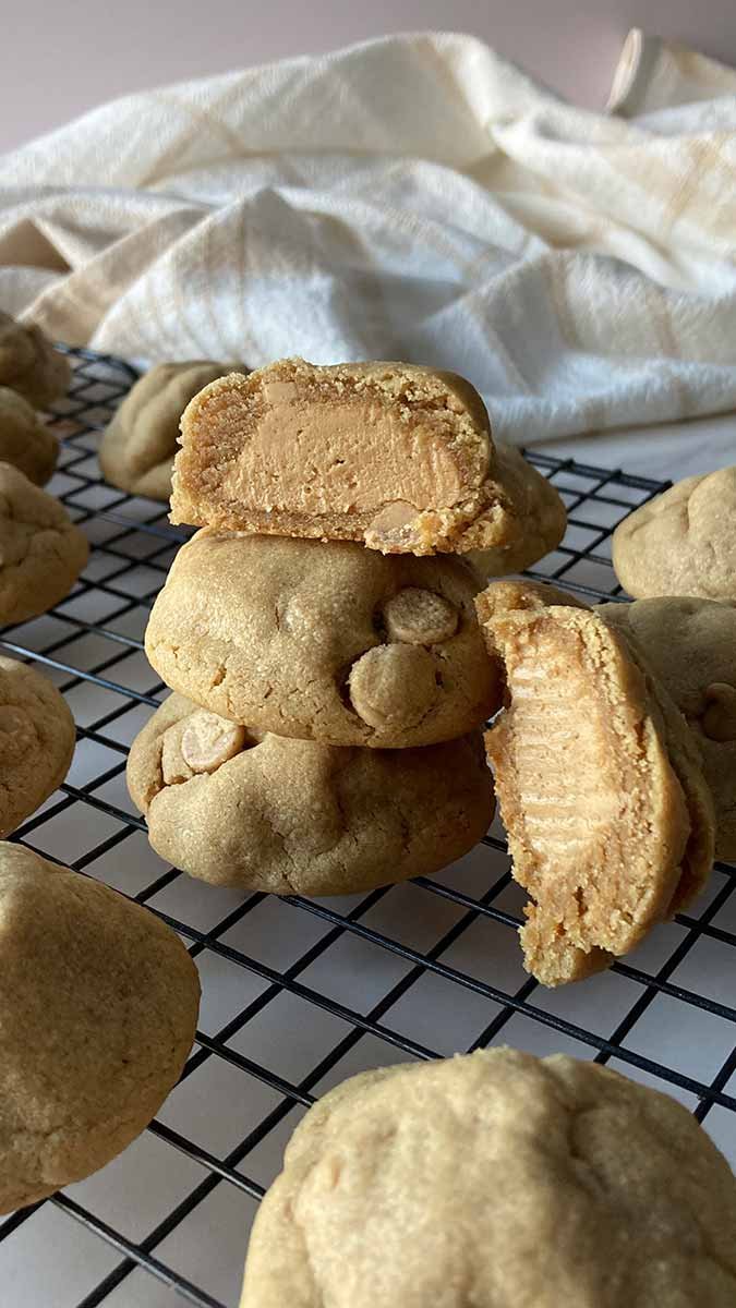 ultimate peanut butter stuffed cookies stacked on cooling rack, one cut open showing peanut butter filled center