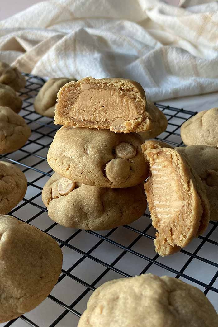 ultimate peanut butter stuffed cookies stacked on cooling rack, one cut open showing peanut butter filled center