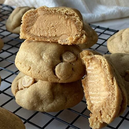 ultimate peanut butter stuffed cookies stacked on cooling rack, one cut open showing peanut butter filled center
