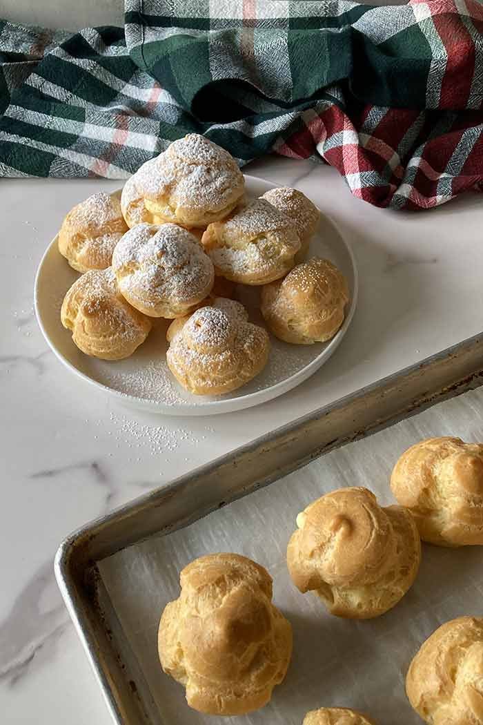homemade cream puffs on a plate and cookie sheet