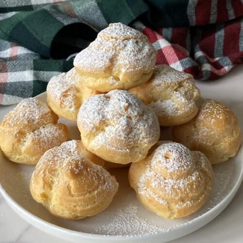 homemade cream puffs dusted with powdered sugar stacked on a plate