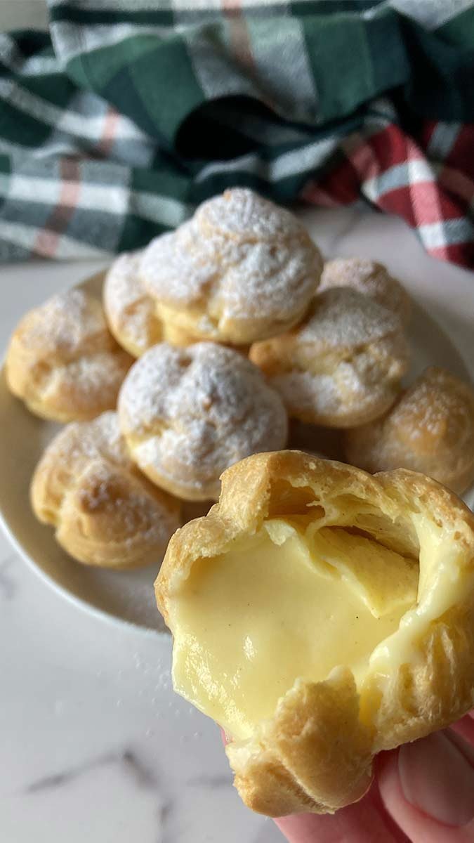 stack of homemade cream puffs with one bitten into to show the pastry cream filling