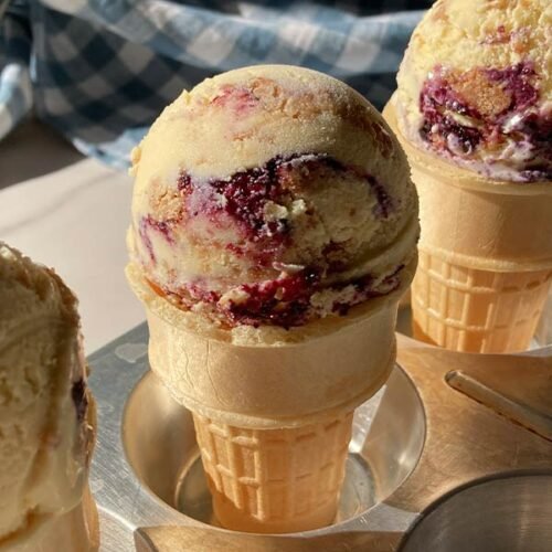 a scoop of blueberry streusel muffin ice cream in each of 3 cones, sitting in a muffin tin