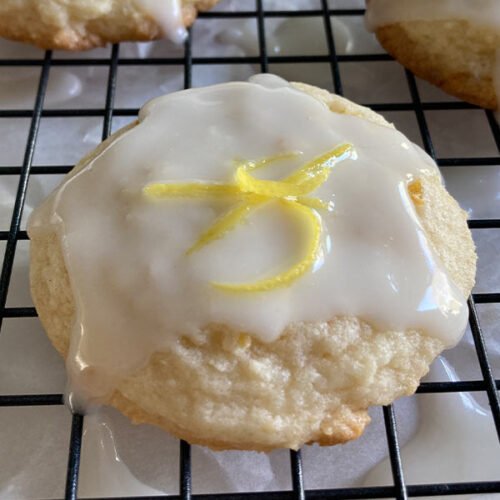 close up of a homemade lemon cookie drizzled with lemon glaze and topped with lemon zest