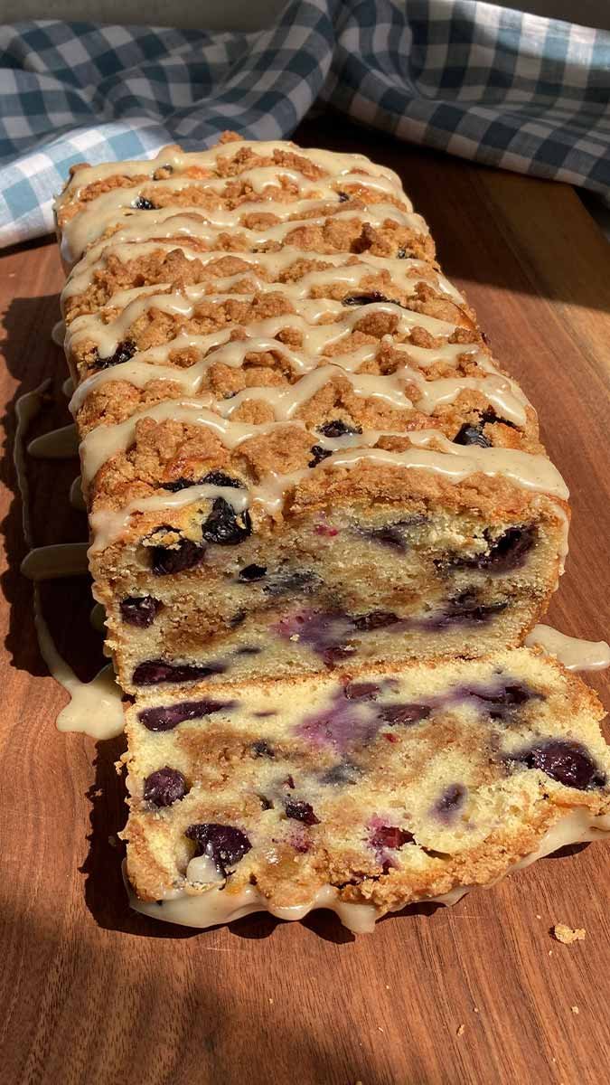 blueberry streusel loaf cake drizzled with glaze, sliced to show the blueberries and cinnamon swirl inside