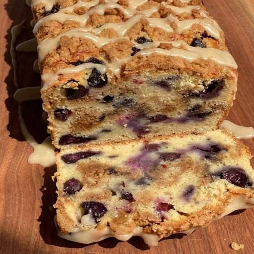 blueberry streusel loaf cake drizzled with glaze, sliced to show the blueberries and cinnamon swirl inside