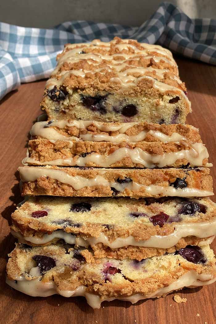 slices of blueberry streusel loaf cake drizzled with glaze on a wooden cutting board
