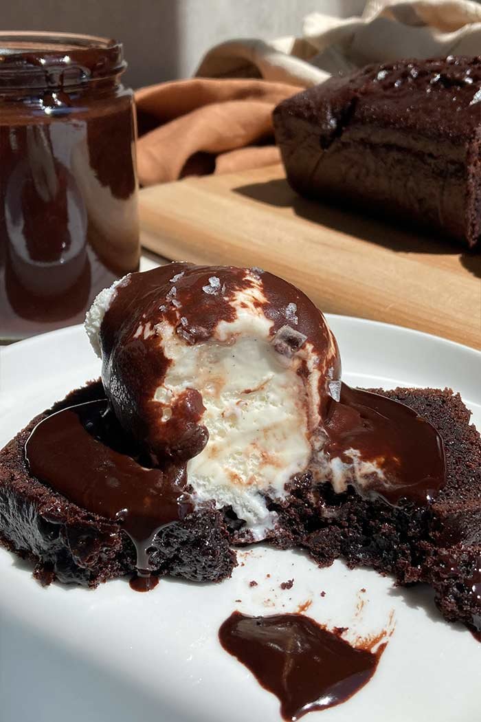 slice of chocolate espresso loaf cake with a scoop of vanilla ice cream, brown butter espresso hot fudge, and flaky salt with a bite taken out to show textures