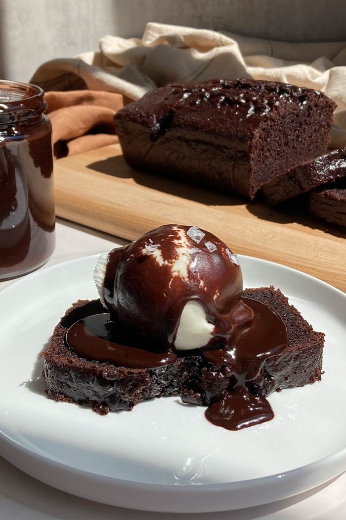 slice of chocolate espresso loaf cake with a scoop of vanilla ice cream, brown butter espresso hot fudge, and flaky salt with the sliced loaf behind