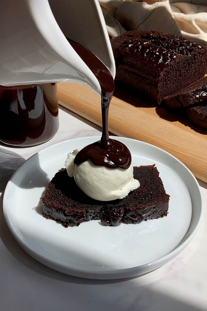 brown butter espresso hot fudge pouring over a slice of chocolate espresso loaf cake with a scoop of vanilla ice cream
