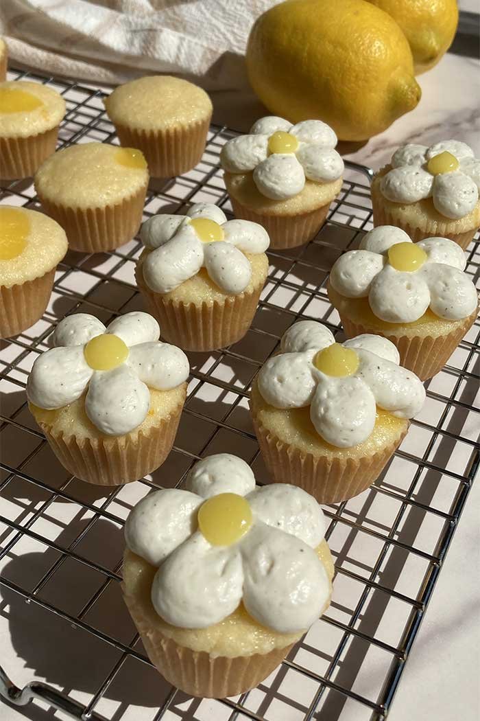 a cooling rack full of mini lemon chantilly cupcakes frosted with whipped cream frosting to look like a flower with lemon curd in the center