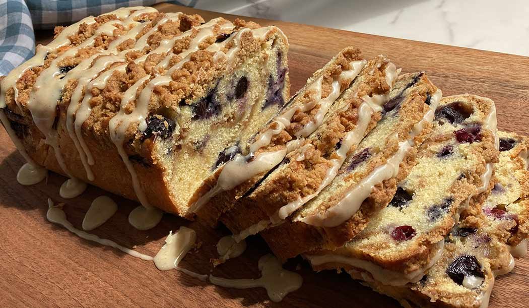 slices of blueberry streusel loaf cake drizzled with glaze on a wooden cutting board