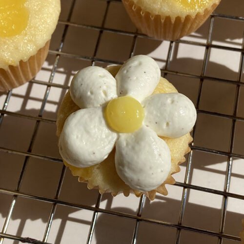 a frosted lemon chantilly cupcake on a cooling rack surrounded by unfrosted cupcakes topped with lemon curd