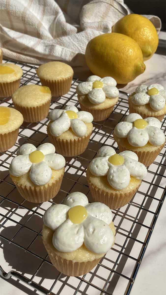 a cooling rack filled with mini lemon chantilly cupcakes frosted with whipped cream and lemon curd in the shape of a flower