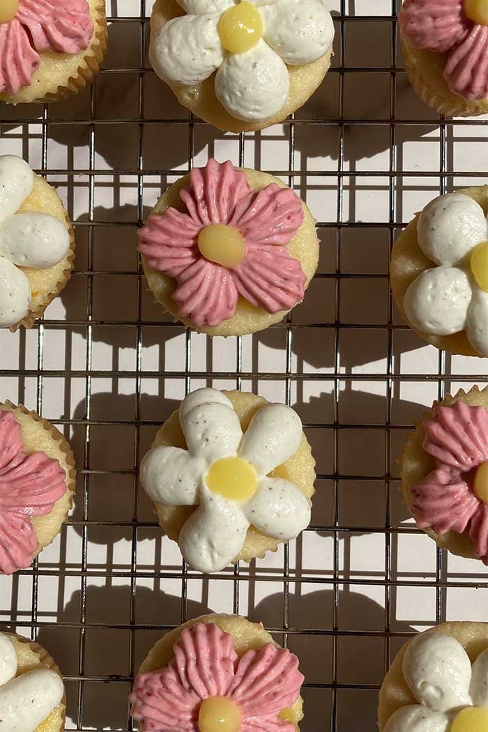 overhead view of a cooling rack filled with mini lemon chantilly cupcakes and raspberry lemonade cupcakes frosted to look like flowers