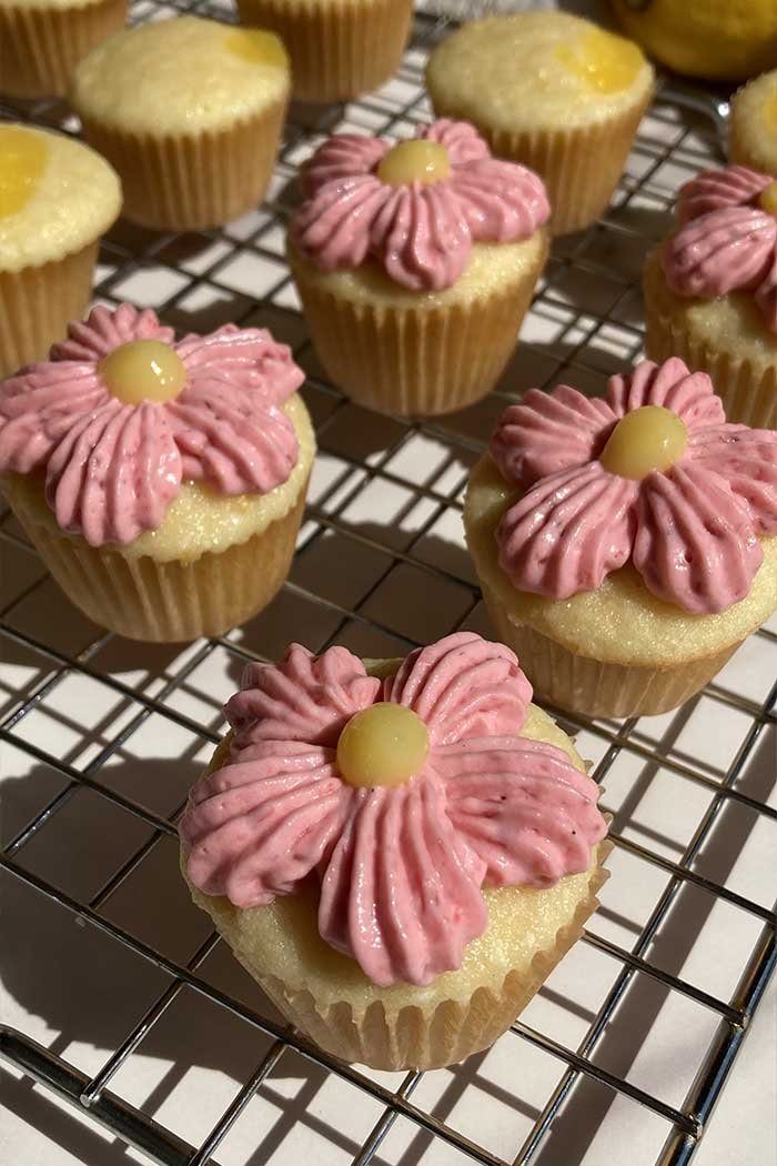 close up of mini raspberry lemonade cupcakes, some decorated like flowers on a cooling rack