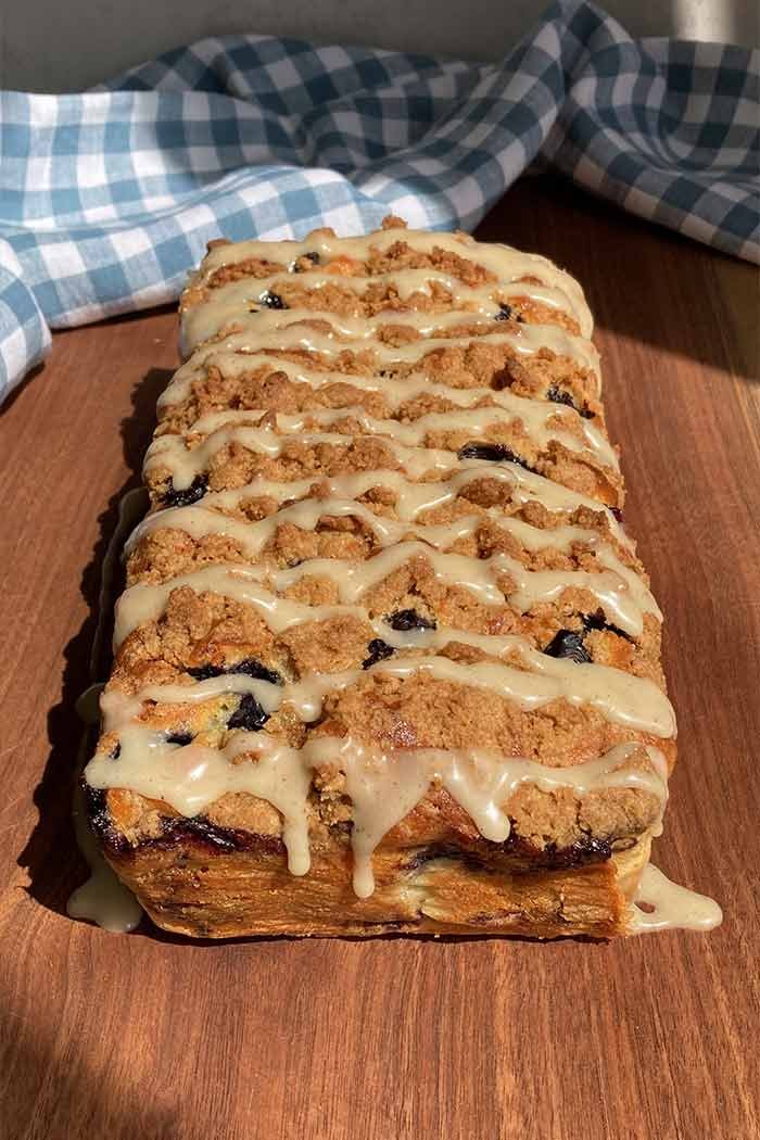 a blueberry loaf cake with cinnamon streusel topping and glaze on a cutting board