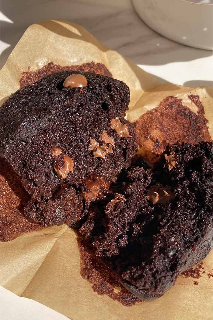 triple chocolate muffin broken in half to show the moist crumb and melty chocolate chips