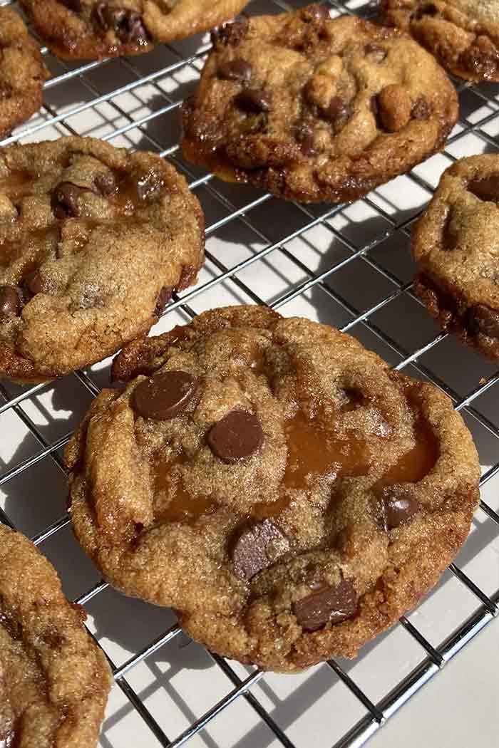 close up of a whole wheat brown butter chocolate chip toffee cookie on a cooling rack showing the melty chocolate chips and puddles of toffee